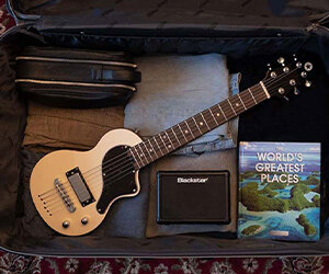 Guitare de voyage Blackstar Carry-On blanche emballée dans un bagage ouvert avec des vêtements pliés et un mini ampli